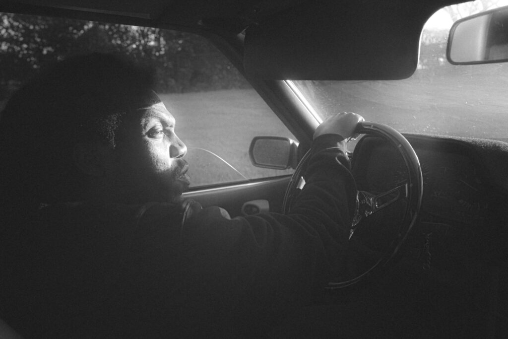 a man sitting in a car with his hand on the steering wheel